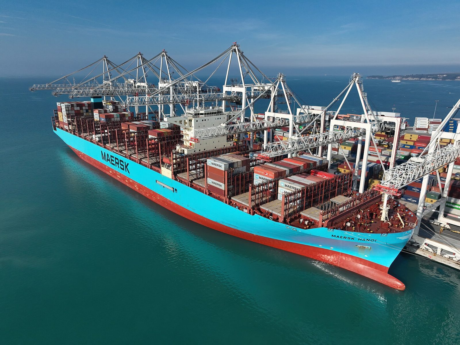Large turquoise Maersk container ship docked beside port cranes