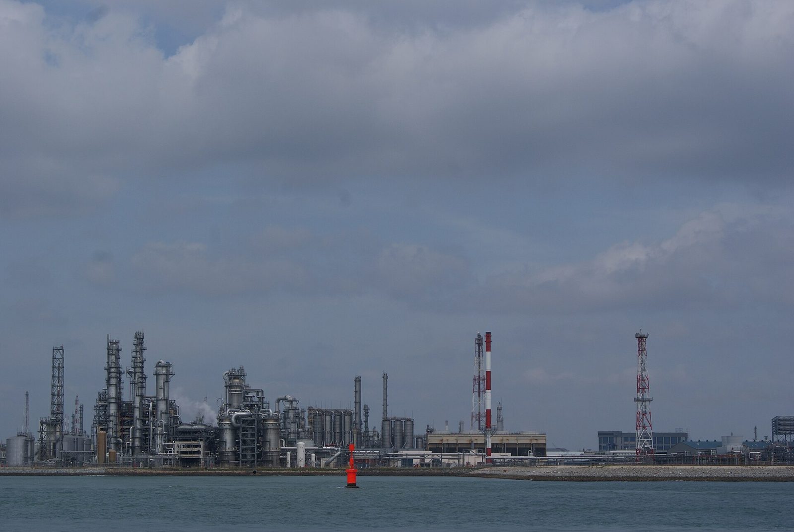 Shoreline refinery structures, tanks and pipework under a cloudy sky