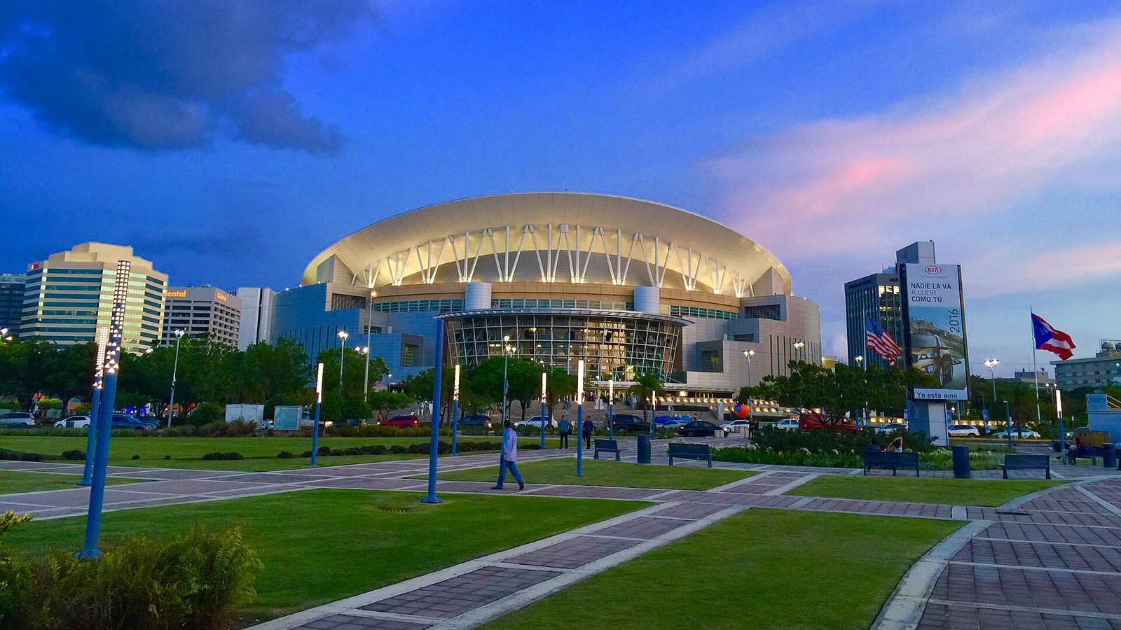 illuminated arena at dusk, park and flags in foreground