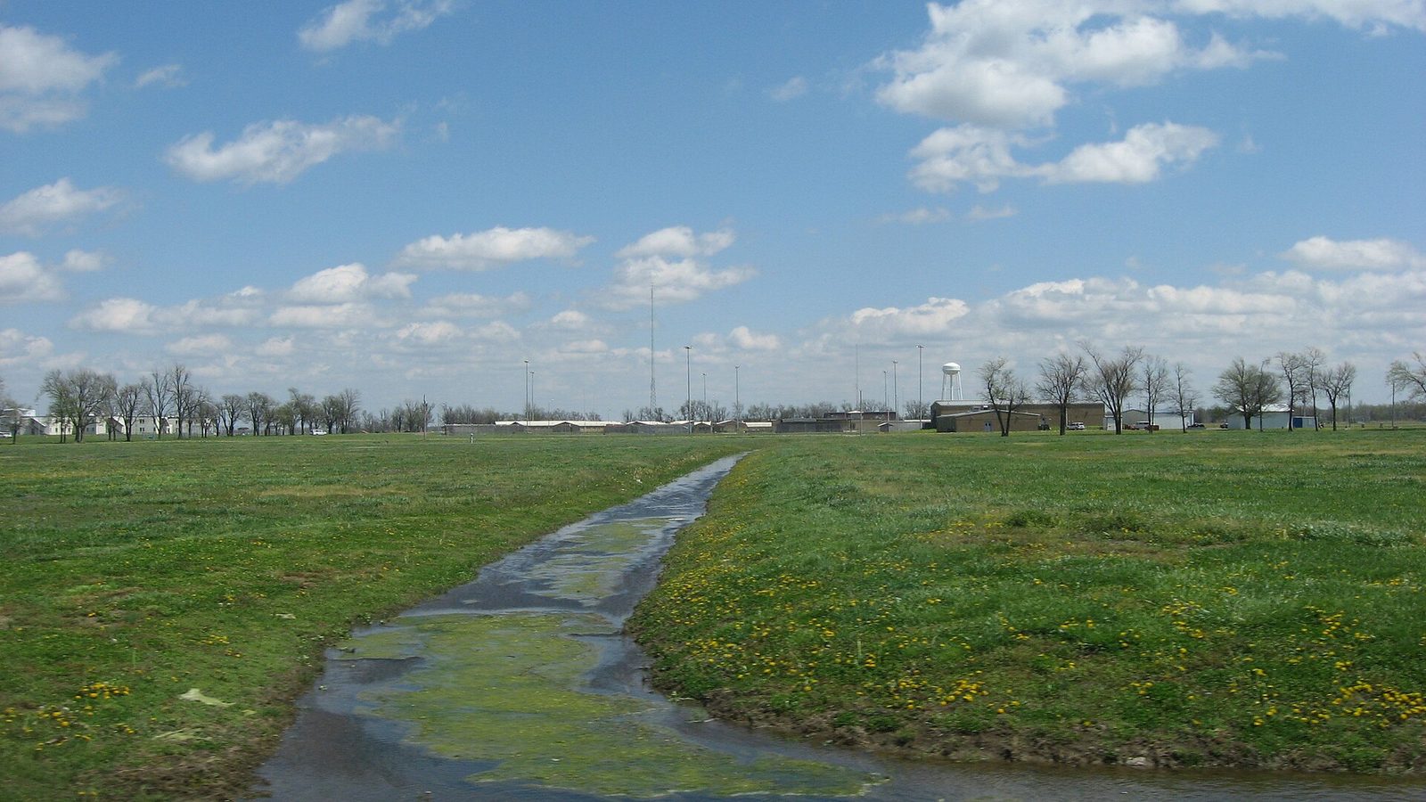 Low brick buildings and water tower behind a grassy field, clear sky, Tiptonville