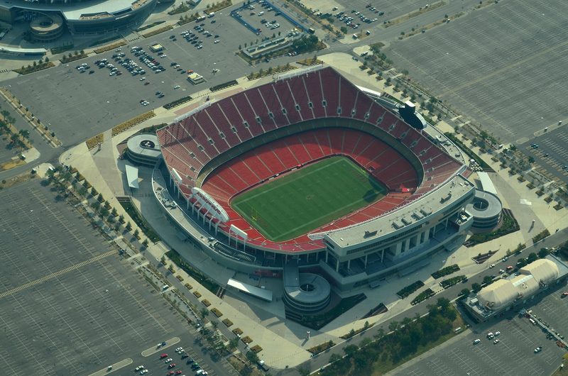 aerial view of a large red-roofed football stadium and surrounding parking, Kansas City