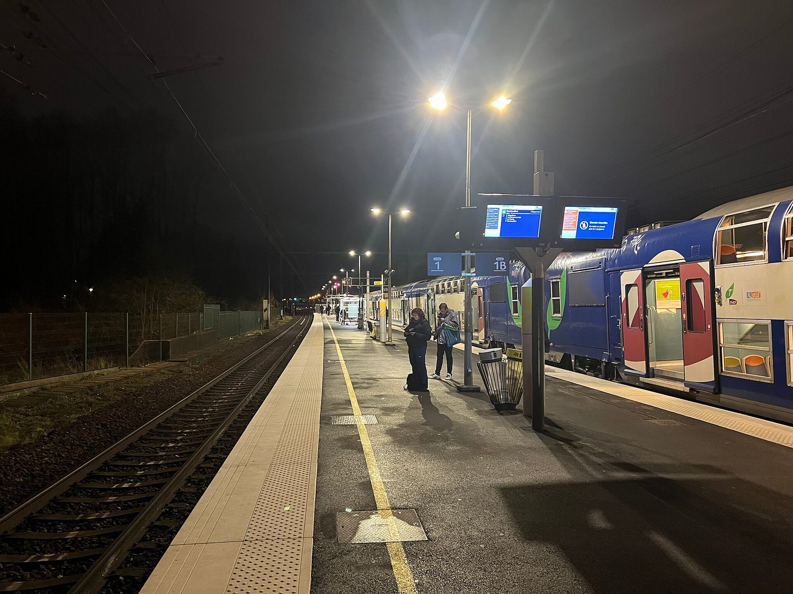 Night train platform with trains and a few commuters waiting