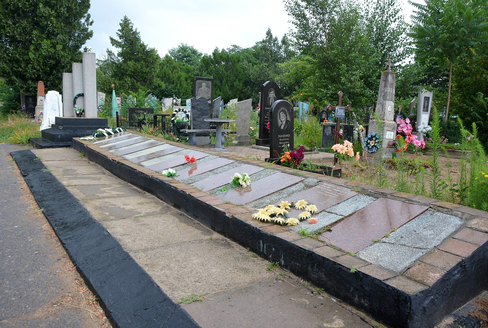 Gravestones and memorial slabs in a cemetery, flowers laid nearby, Oleshky