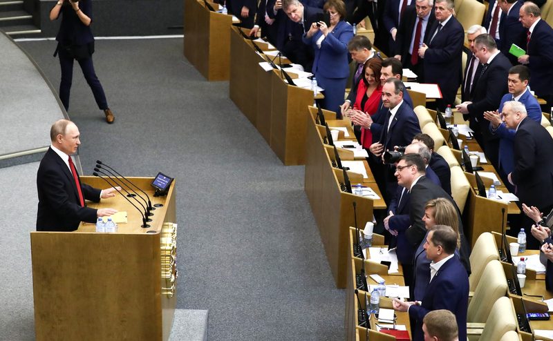 man speaking at wooden podium to standing assembly of officials