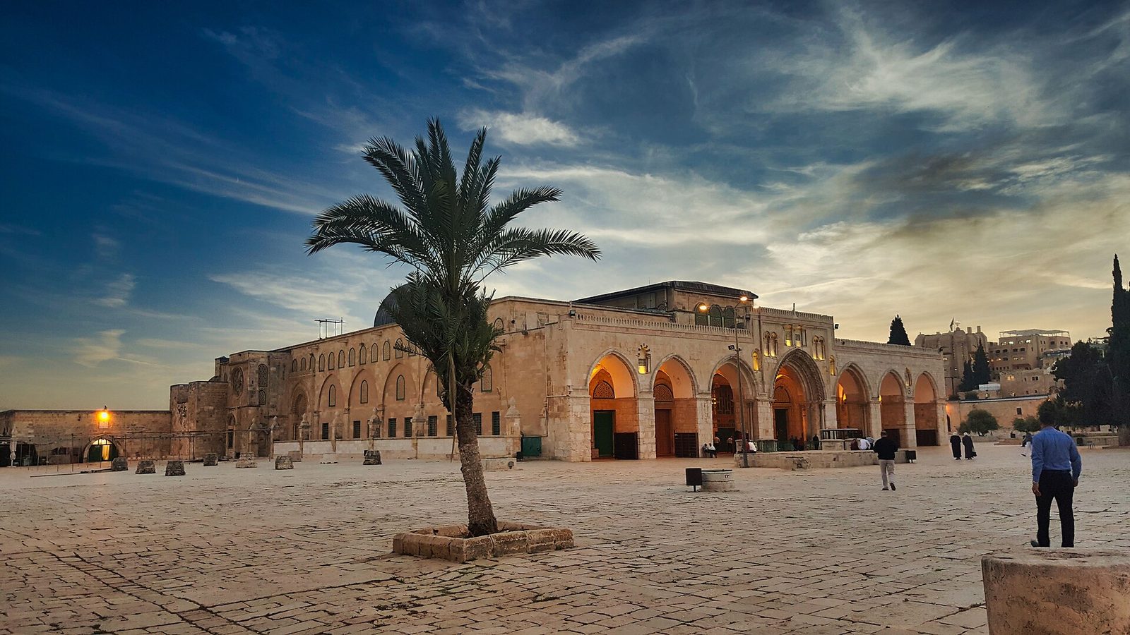 Al-Aqsa Mosque exterior at dusk, palm tree in the foreground