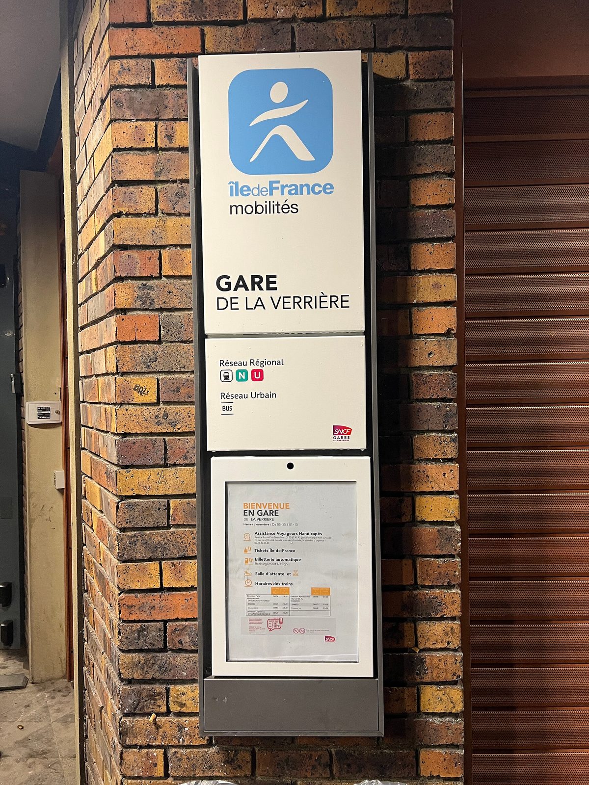 Tall totem sign reading 'GARE DE LA VERRIÈRE' on brick wall