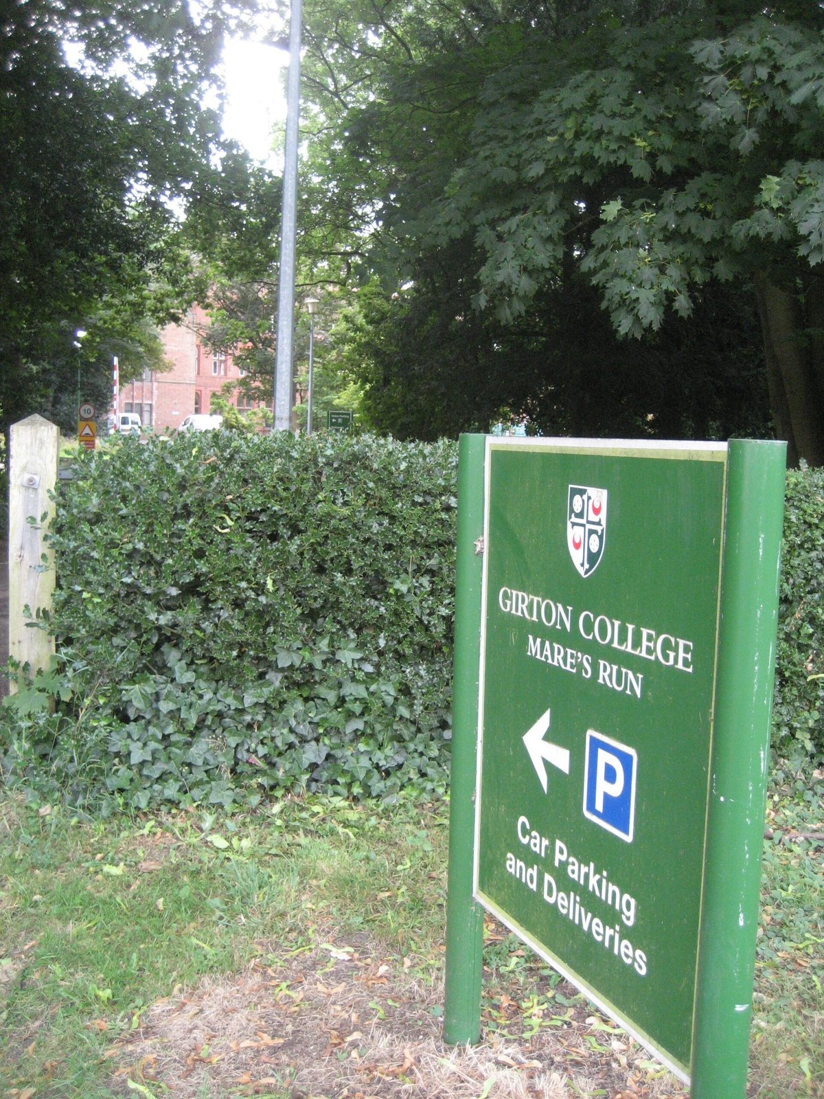 Green directional sign reading GIRTON COLLEGE, hedges and trees, Girton College
