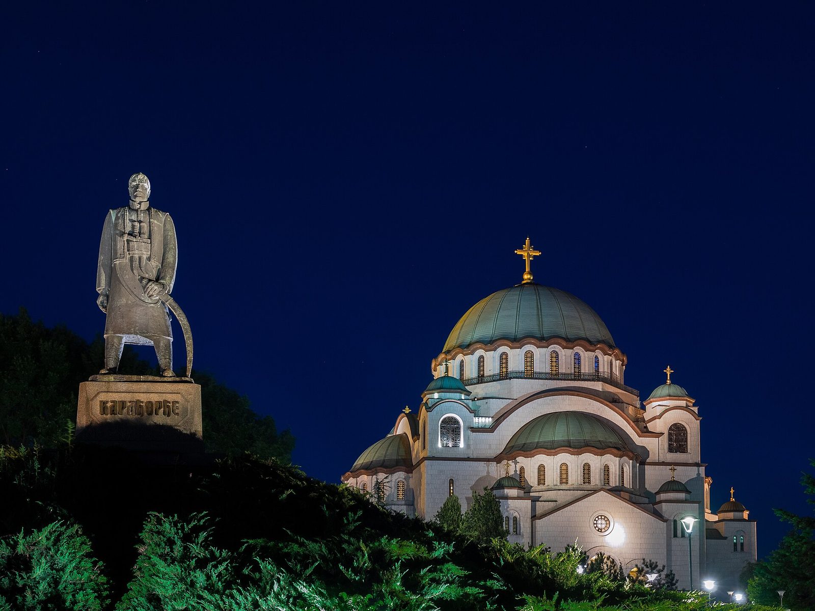 Large domed church illuminated at night, statue silhouetted in foreground