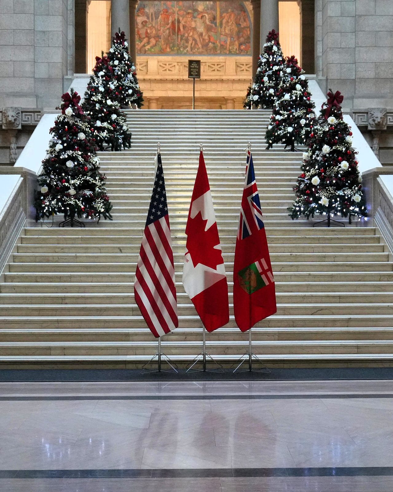 Three flags including US and Canadian flags on marble steps with trees