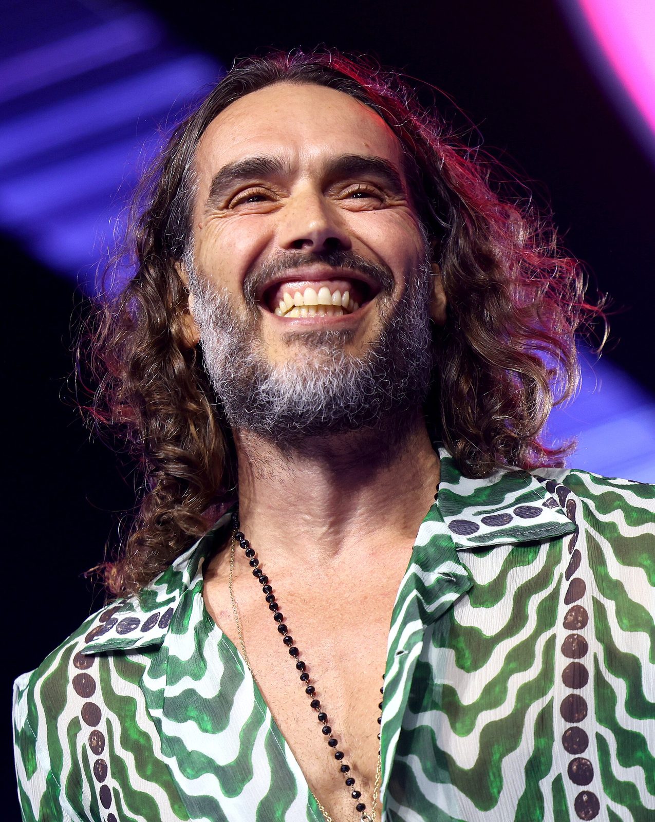 Close-up smiling man on stage, patterned shirt, long hair and beard