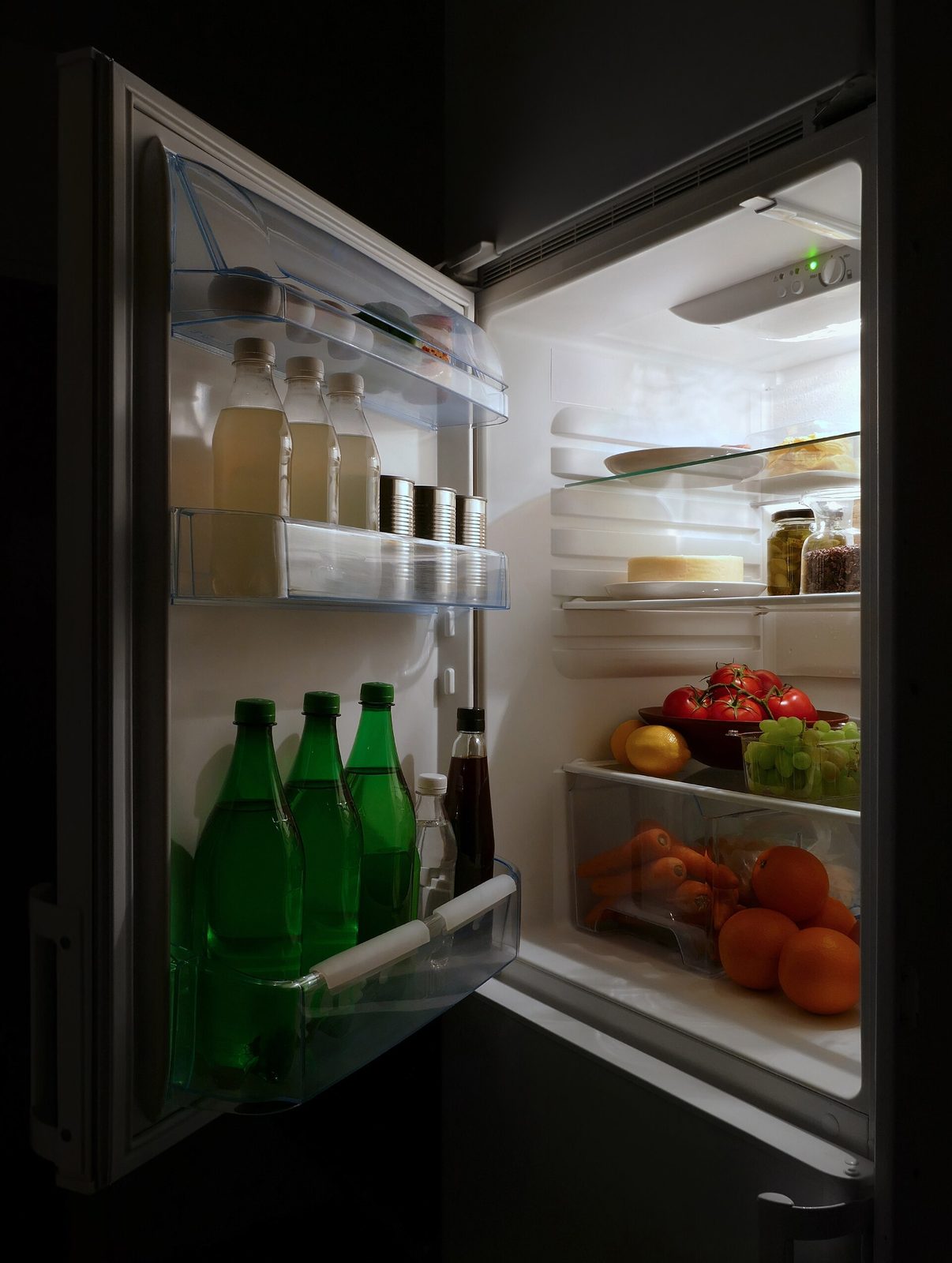 Open domestic refrigerator showing bottles, tins, fruit and vegetables