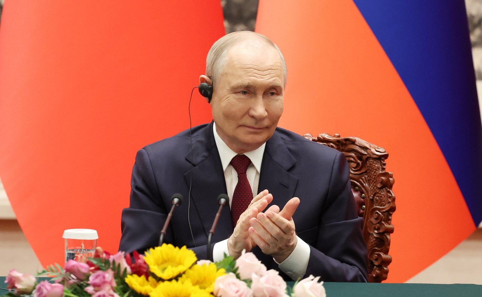 Man in suit clapping, red and blue flags behind him