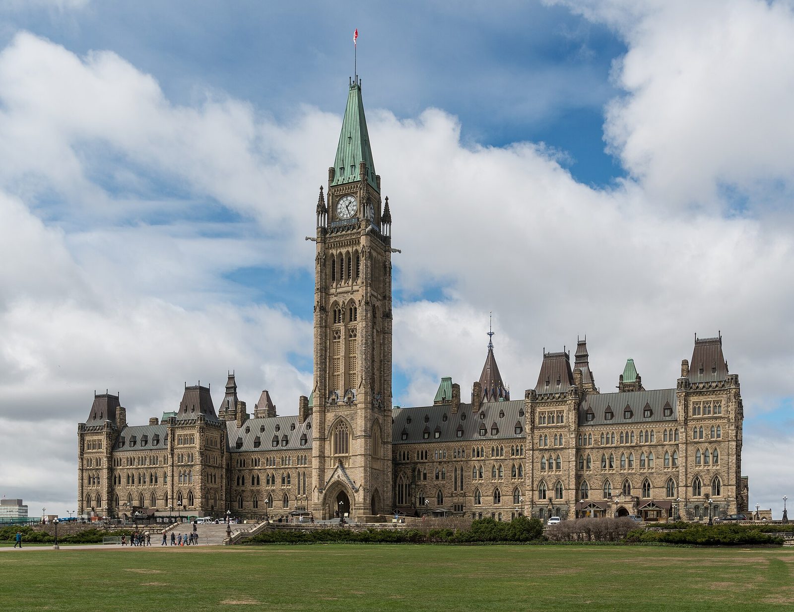 Large gothic stone parliamentary building with tall clock tower and lawn, Ottawa