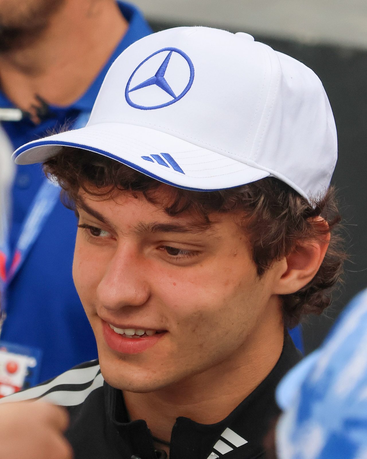 Close-up of a young man smiling, wearing white cap with Mercedes logo