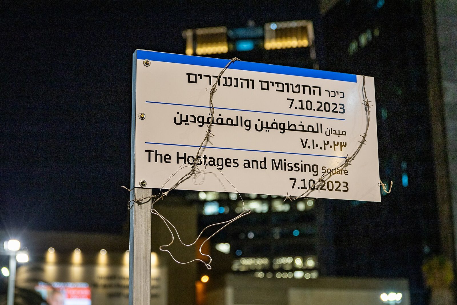 White sign reading 'The Hostages and Missing Square' with barbed wire, Tel Aviv