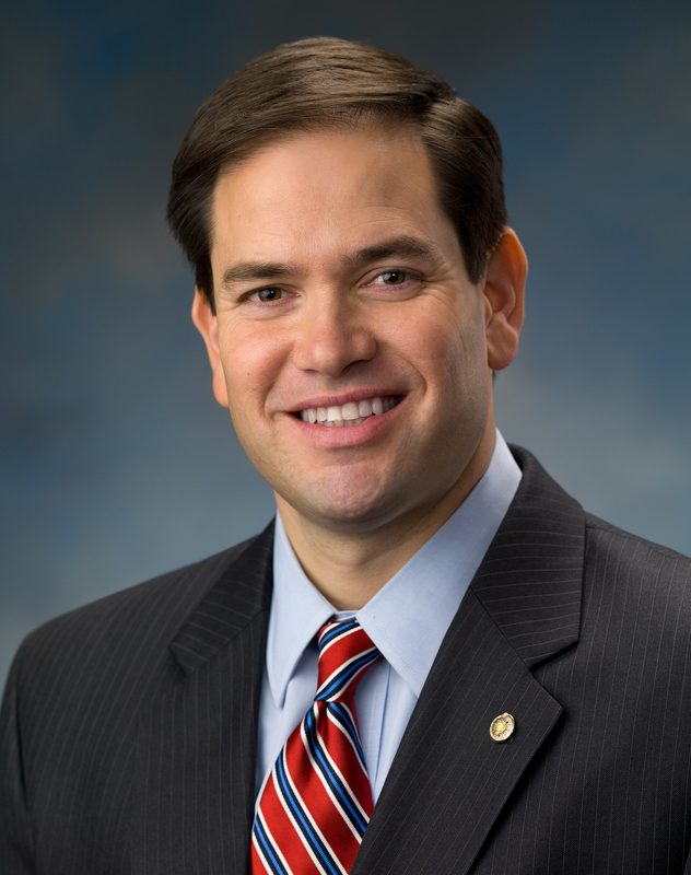 Smiling man in suit, striped tie, neutral studio backdrop.