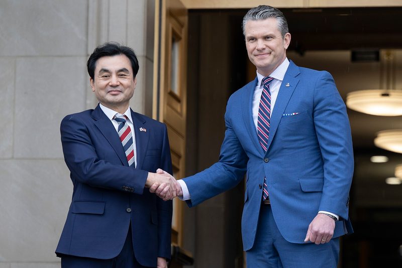 Two men in suits shaking hands at building entrance, honour guards present