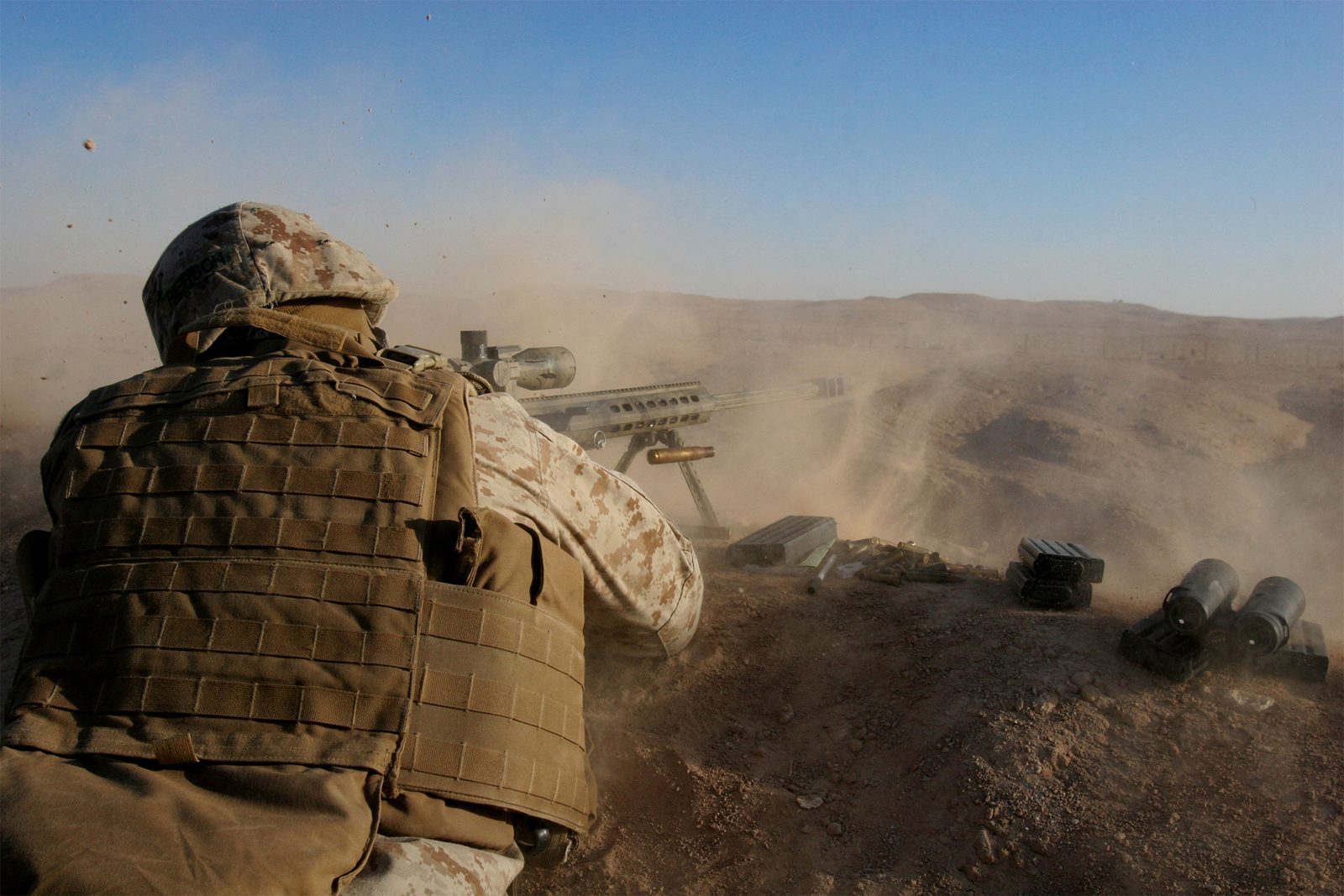 Soldier firing a large-calibre sniper rifle from a dusty desert position