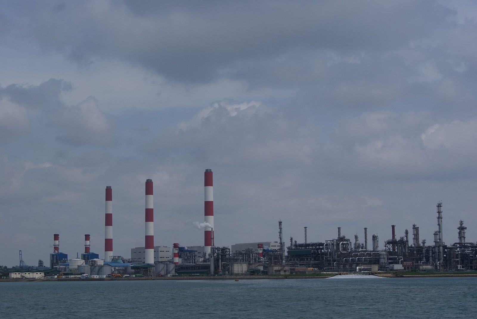 Industrial oil and chemical plants on shoreline, tall red-and-white chimneys