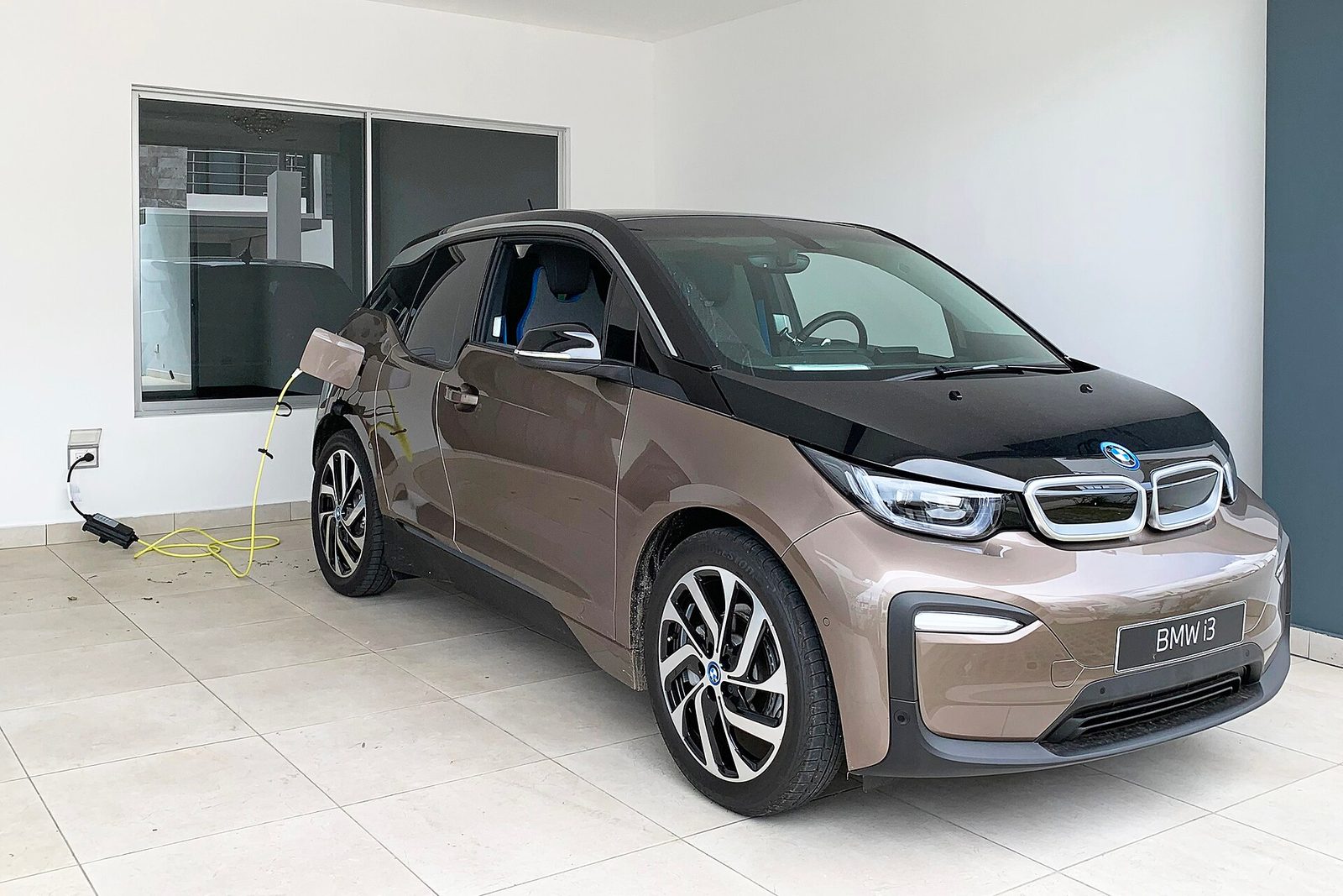 Small electric car parked in garage, yellow cable plugged into home wall