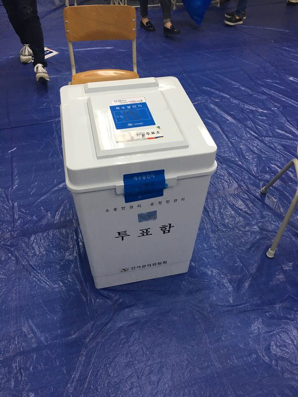 white plastic ballot box on blue tarp inside polling place