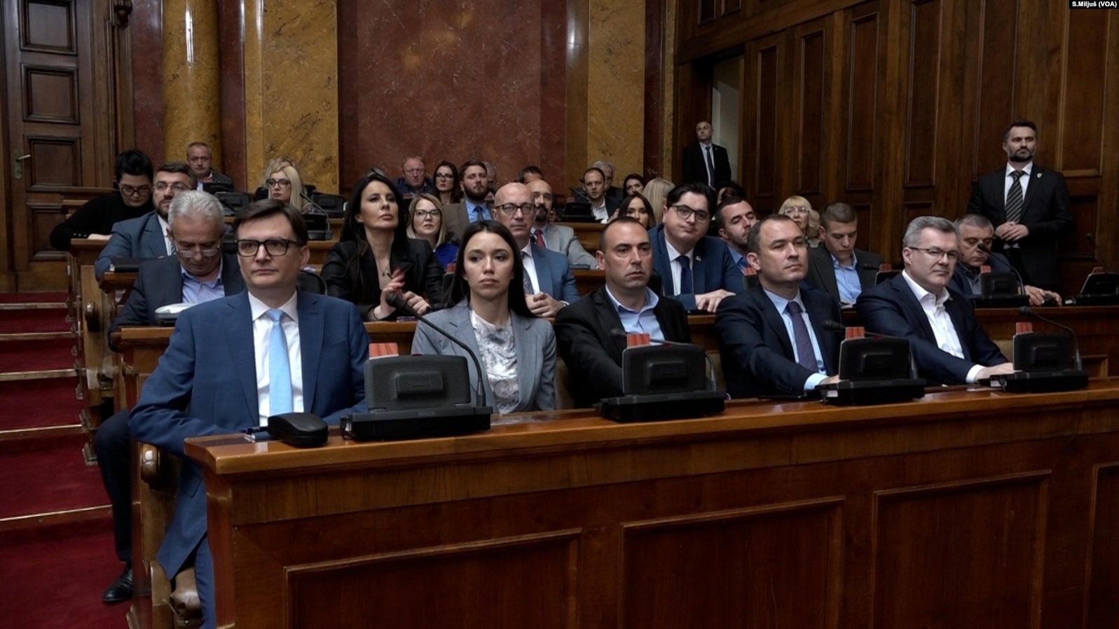 People seated in a parliamentary chamber, rows of desks and microphones.