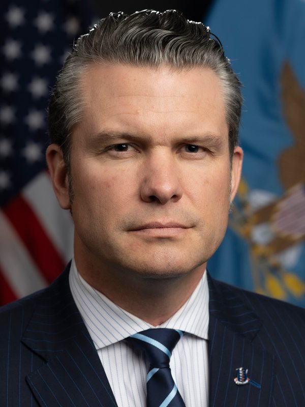 Close-up official portrait of a man in suit, flags behind.
