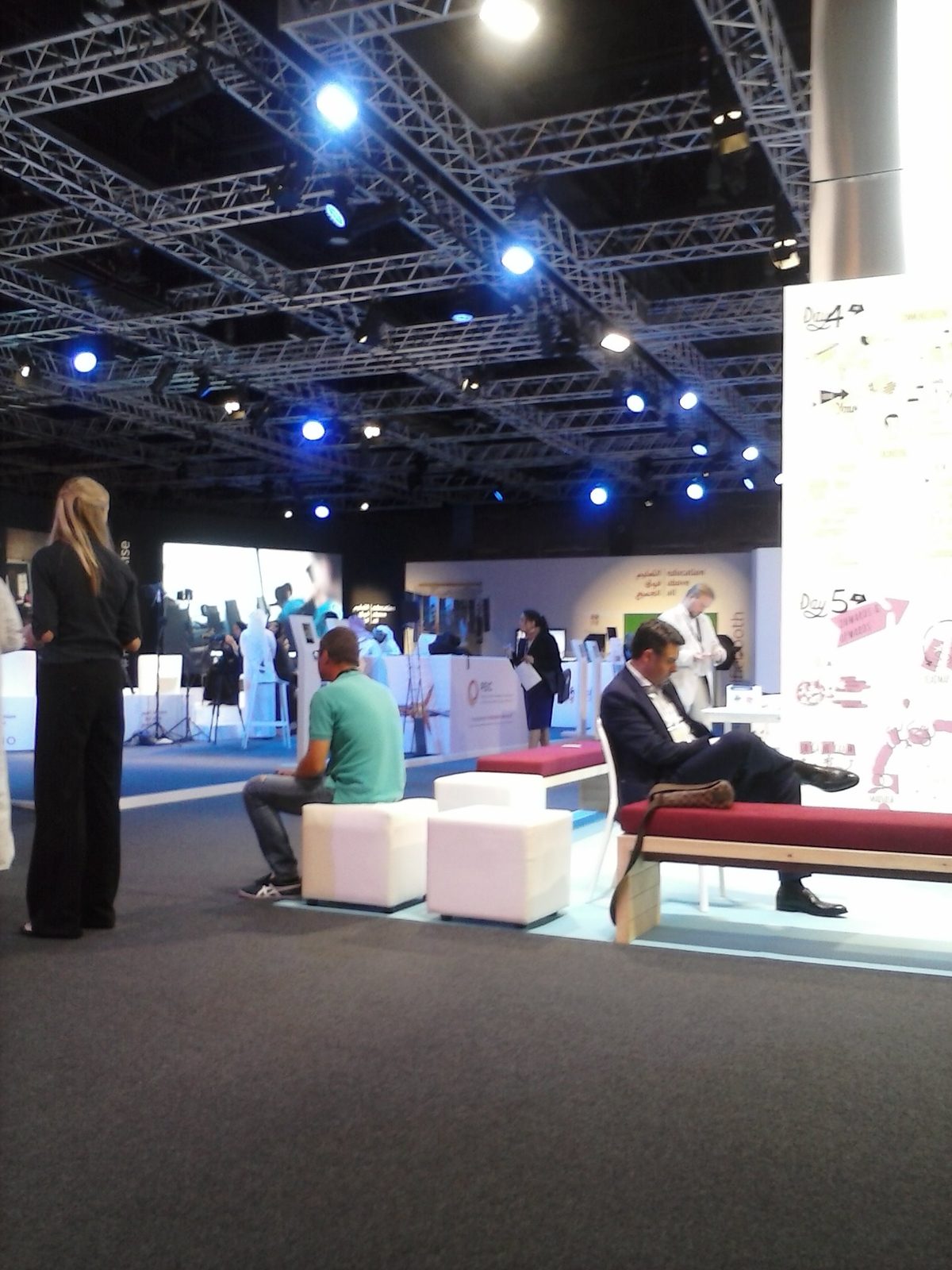 Open conference area with whiteboards, benches, people and blue spotlights, Doha