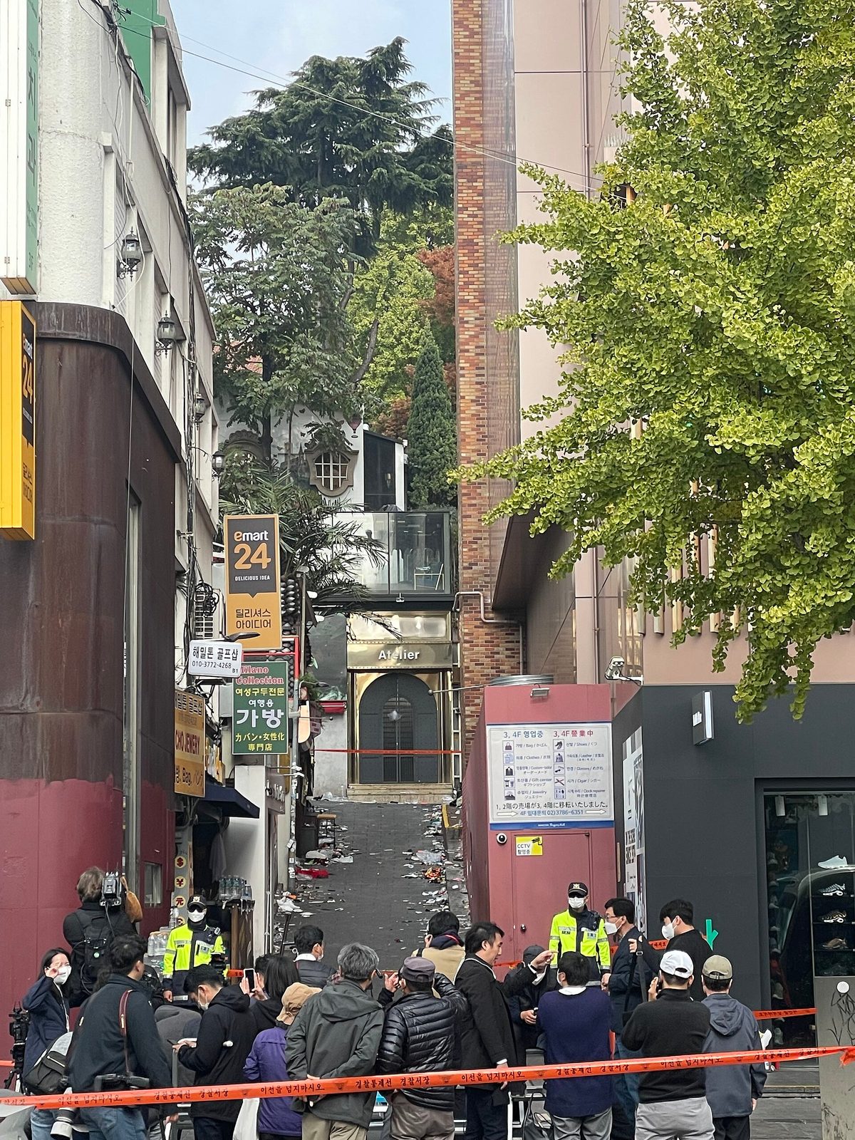 narrow alley with police tape, officers, crowd and littered street, Itaewon
