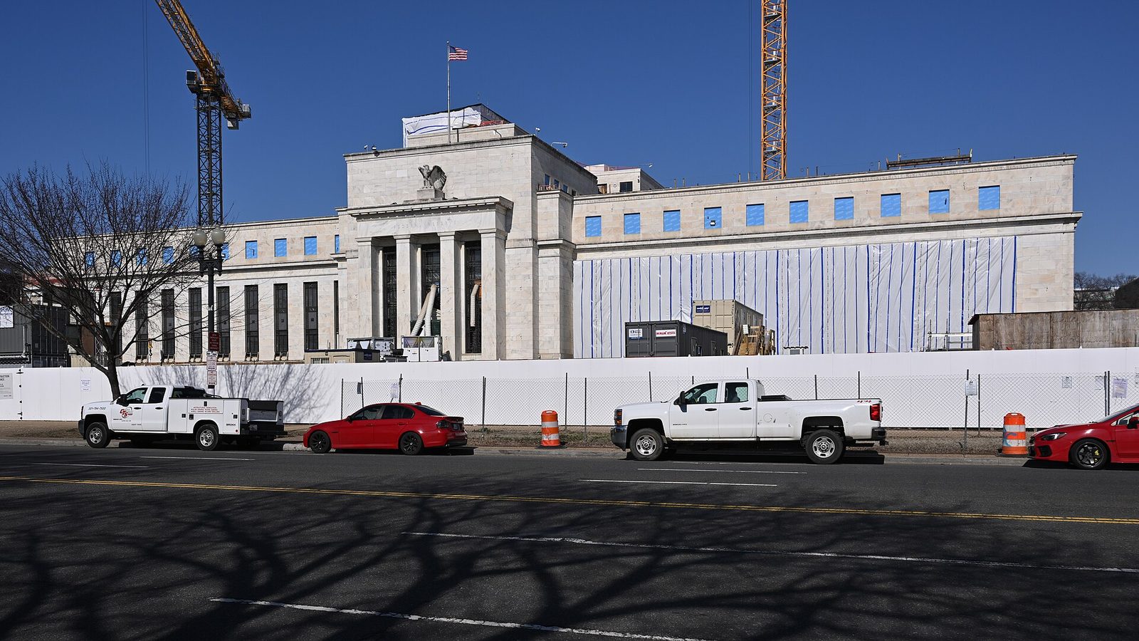 Same white building facade behind construction fencing and parked vehicles, United States